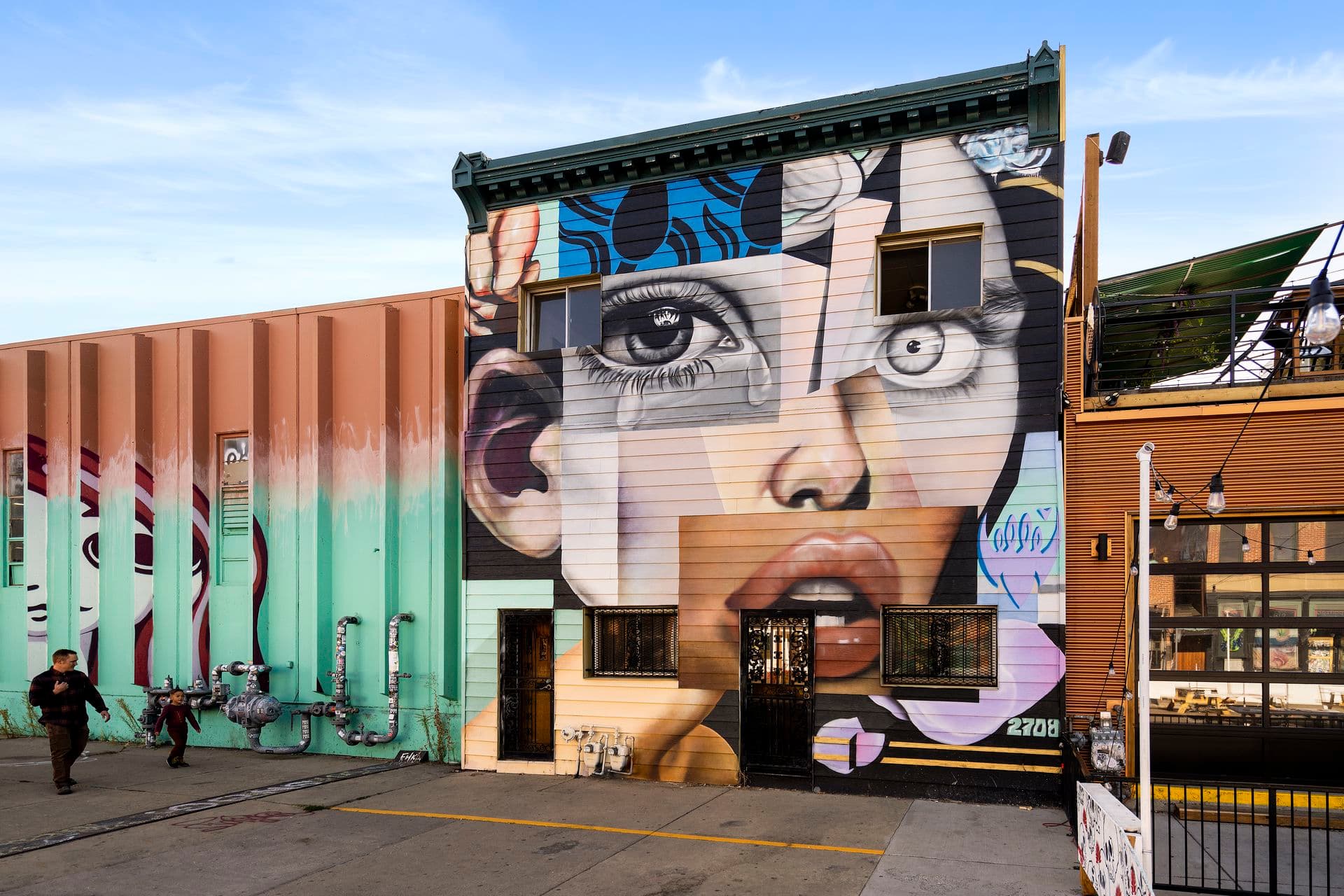 A large mural of a face painted across a building facade in RiNo, Denver, with more murals along the adjacent wall