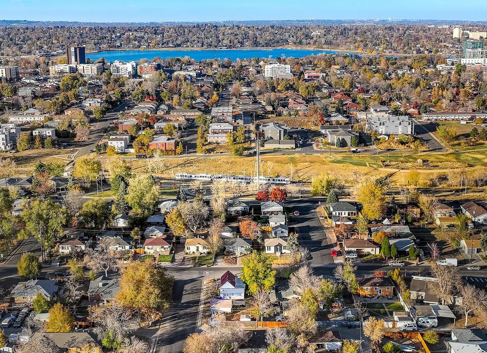 An aerial view of West Colfax, Denver, with a W Line train crossing the neighborhood and Sloan's Lake beyond